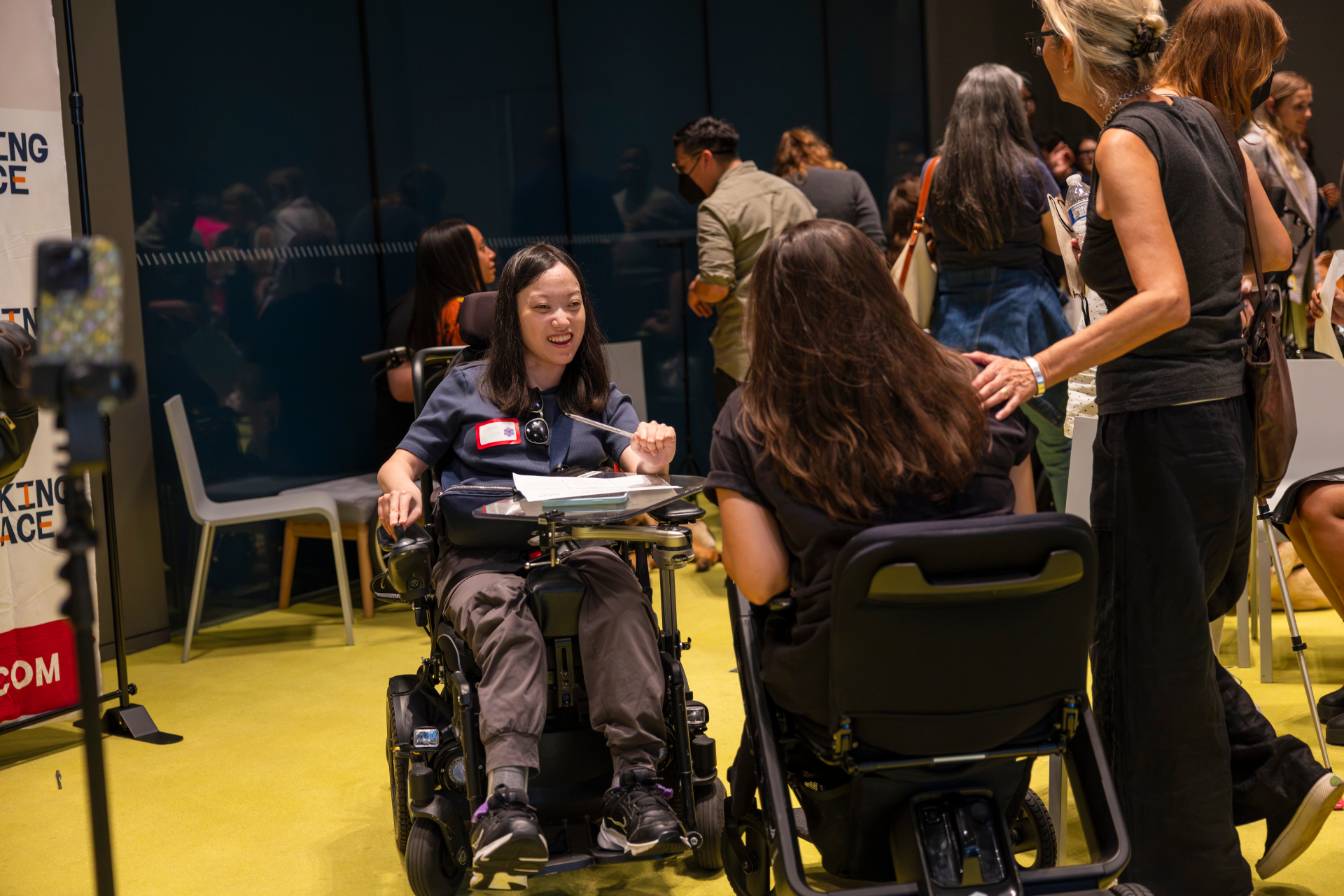 Two attendees in power wheelchairs talking and smiling beside a Making Space banner.